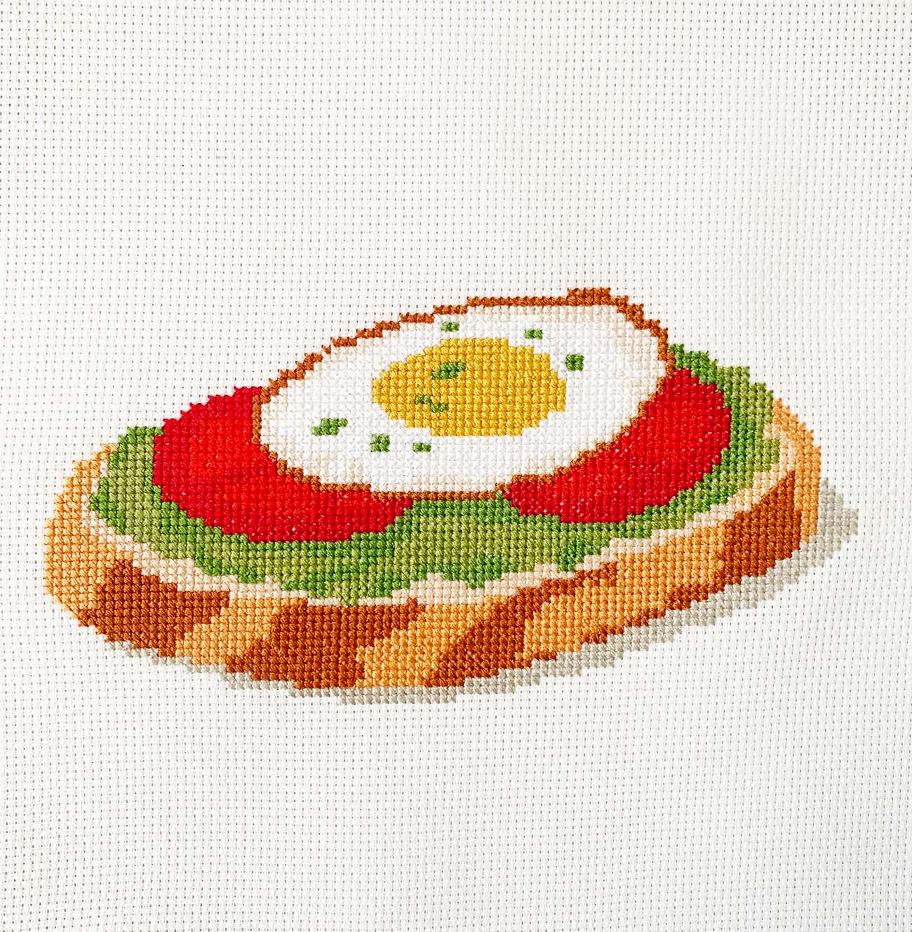 Toast with avocado, tomato, and egg cross stitch showing full stitched design.