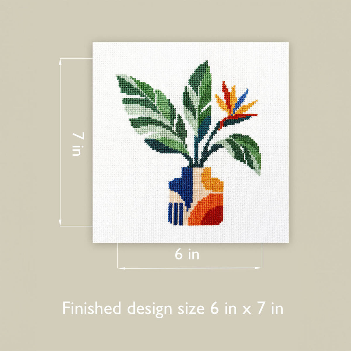 A finished cross-stitch design of a potted plant with green leaves and a colorful bird-of-paradise flower in a geometric vase, shown on a white square canvas against a beige background with dimension labels of 6 in by 7 in and text reading 'Finished design size 6 in x 7 in'.