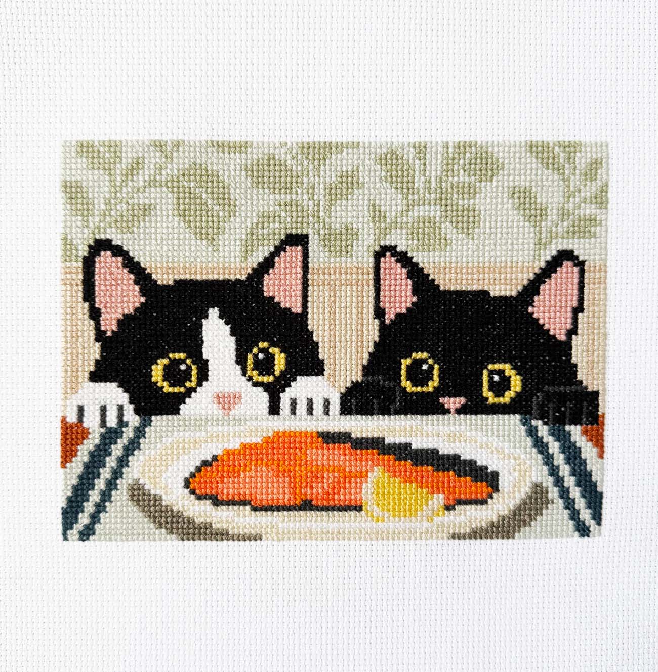 Modern tuxedo cat counted cross stitch kit with two curious black cats peeking over the table at a salmon dinner. Beginner-friendly cat cross stitch pattern for cat lovers and modern home decor.