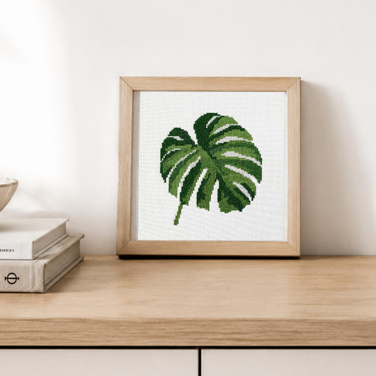 Framed cross-stitched leaf artwork on a wooden surface
