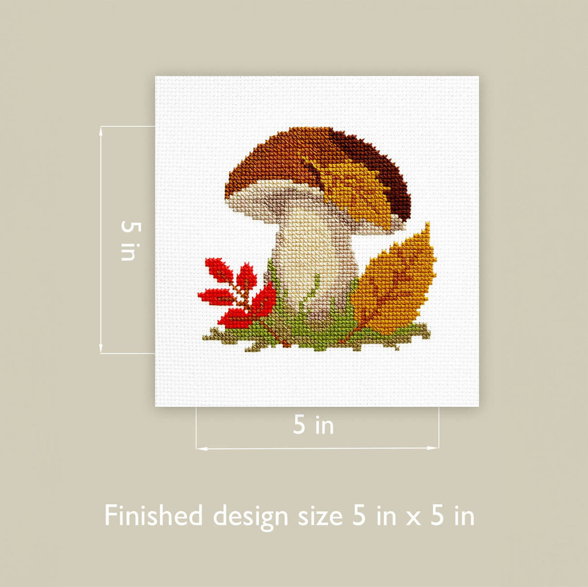 A 5 in x 5 in finished cross-stitch design featuring a mushroom with brown and orange caps, a cream stem, green and red foliage, and an orange leaf on a white fabric square, shown with dimension labels and the text 'Finished design size 5 in x 5 in' on a beige background.