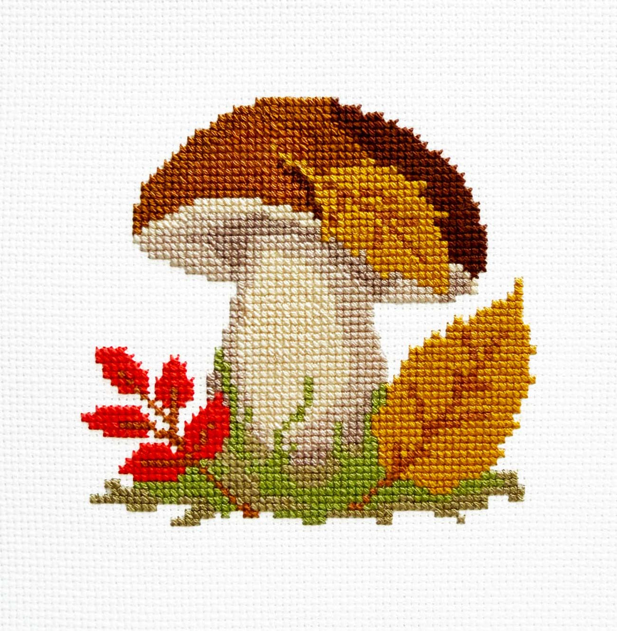 A cross-stitch mushroom design with a brown and cream cap, white stem, green and yellow leaves, and small red leaves on a white Aida fabric background.