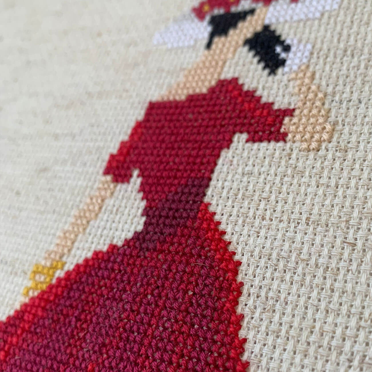 Cross-stitched design of a woman in a red dress on beige fabric