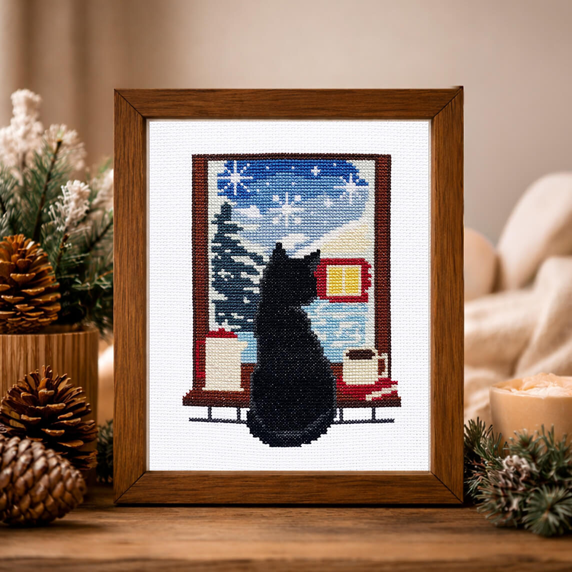 Winter Cat cross stitch kit framed on a wooden table, featuring a black cat looking out a snowy window.