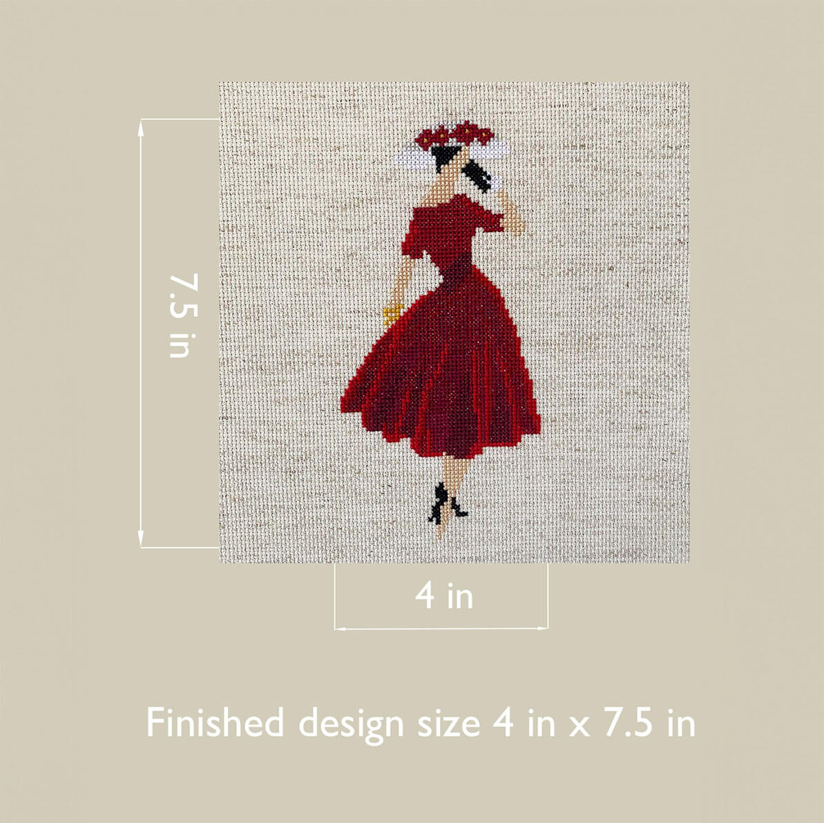 Cross-stitched design of a woman in a red dress on fabric with measurements indicated.