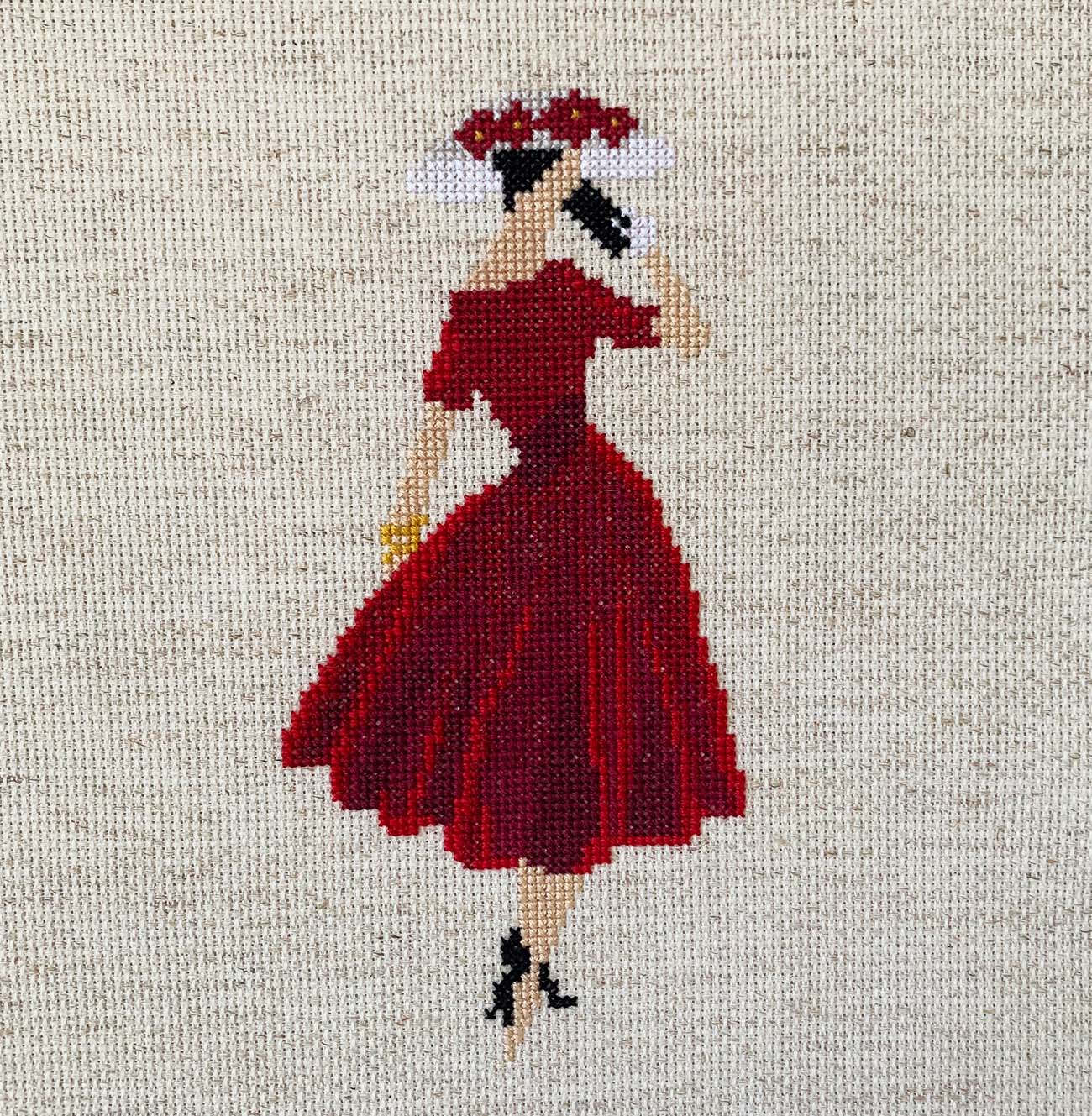 Cross-stitched design of a woman in a red dress on fabric