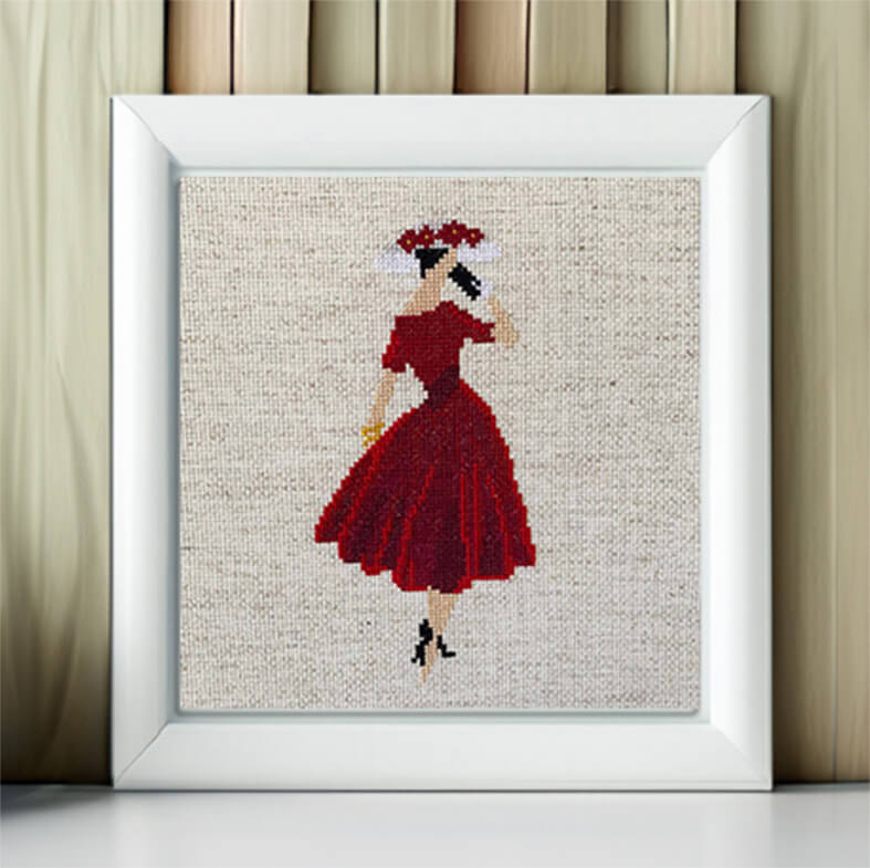 Framed cross-stitched artwork of a woman in a red dress on a neutral background