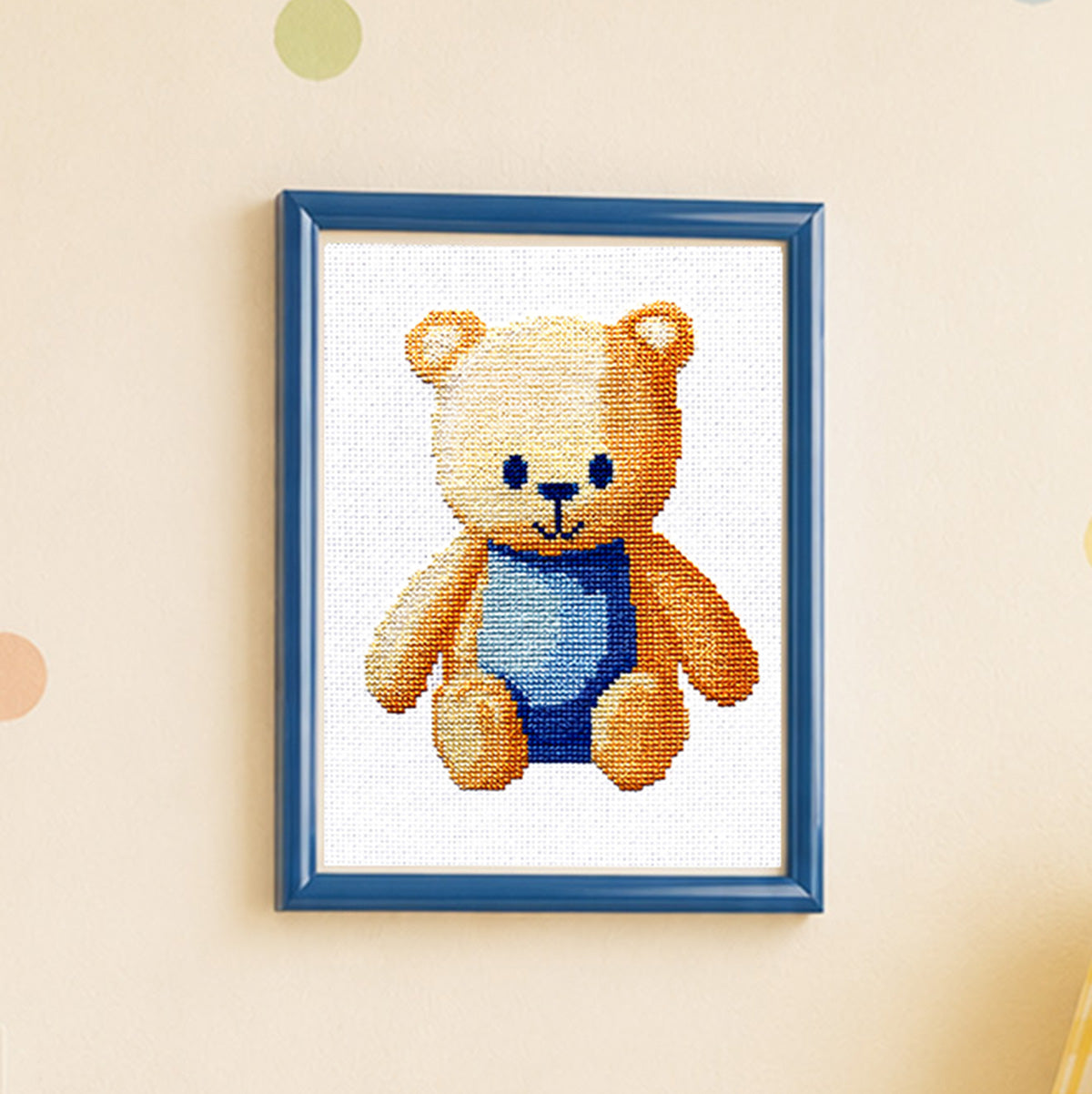 Framed cross-stitched teddy bear on a beige wall
